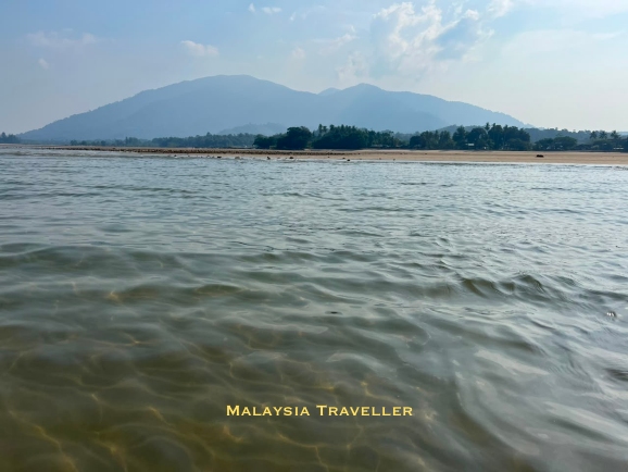 shallow calm sea with beach and mountain in the background